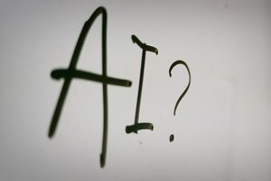 The letters “AI?” handwritten in black marker on a whiteboard