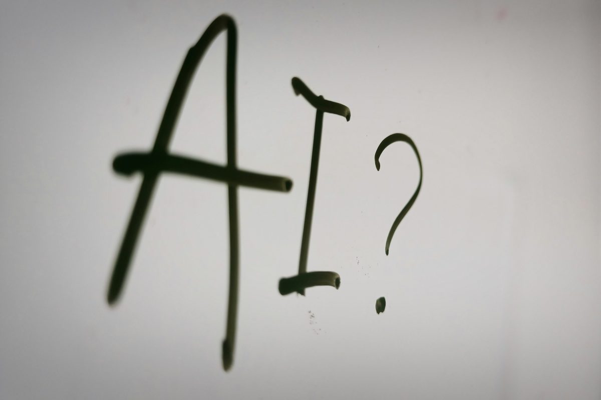 The letters “AI?” handwritten in black marker on a whiteboard