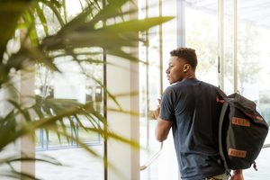 A man with a backpack pushing open a glass door as he leaves an office